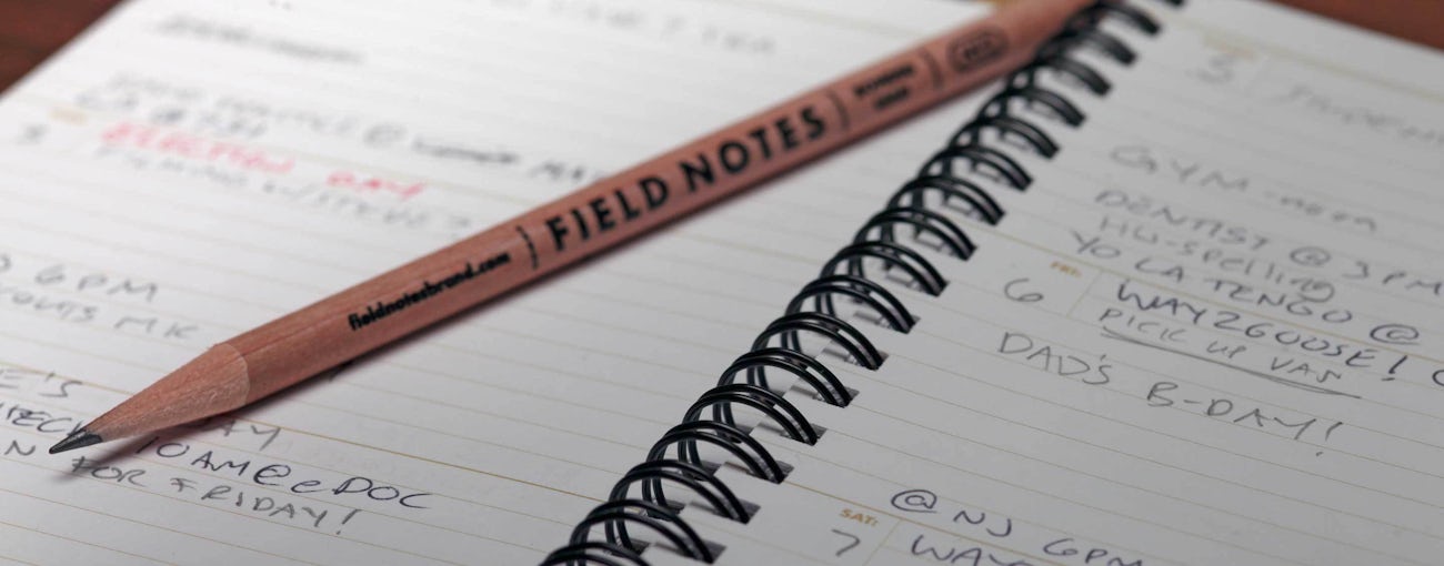 Close up of an open planner with a pencil and events written on the pages.